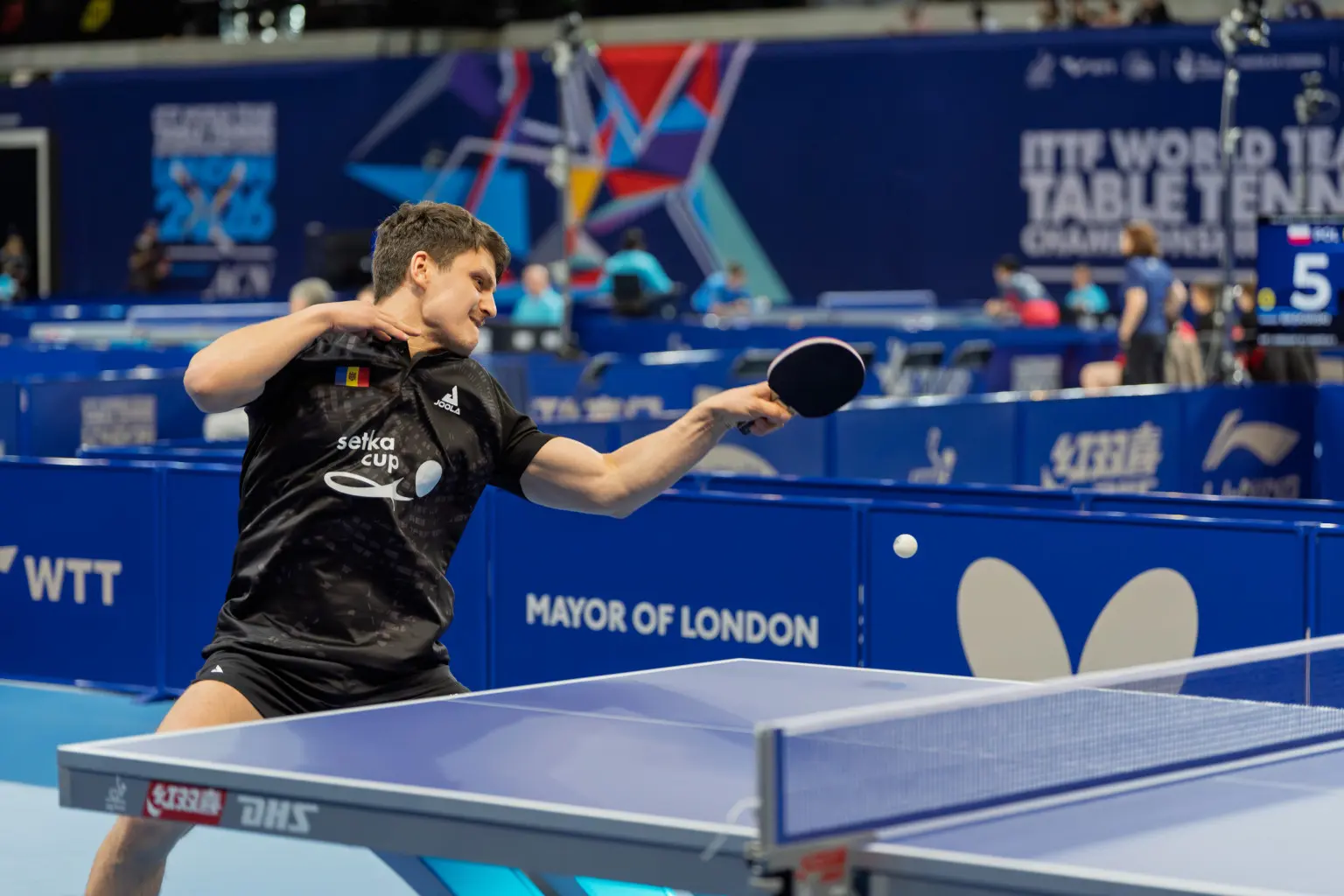 Table tennis player wearing a Setka Cup shirt gestures with his paddle at the 2026 World Team Championships in London.