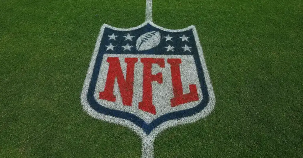 NFL logo painted at midfield on a green American football field viewed from above