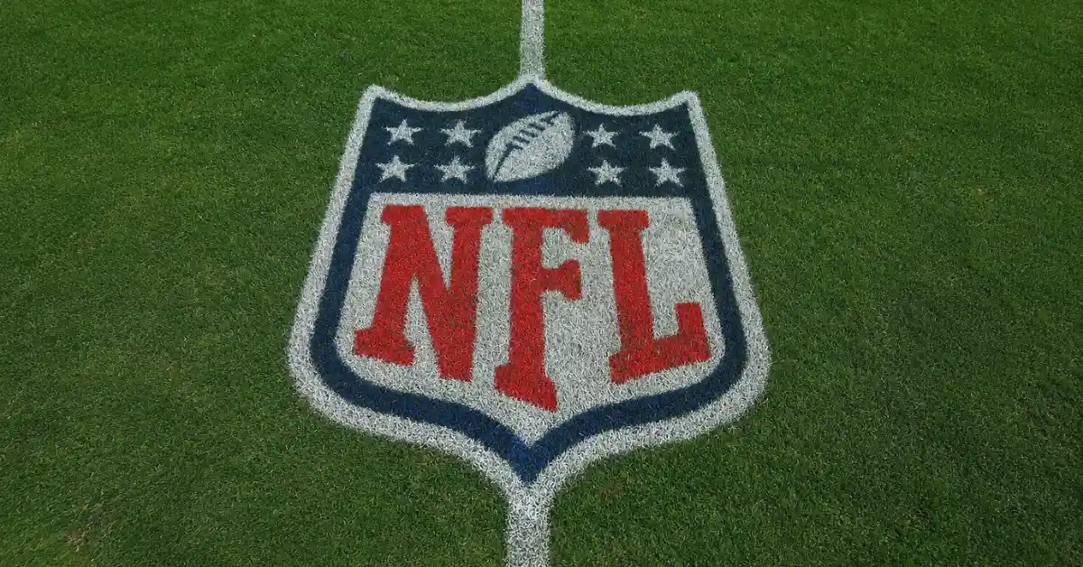 NFL logo painted at midfield on a green American football field viewed from above