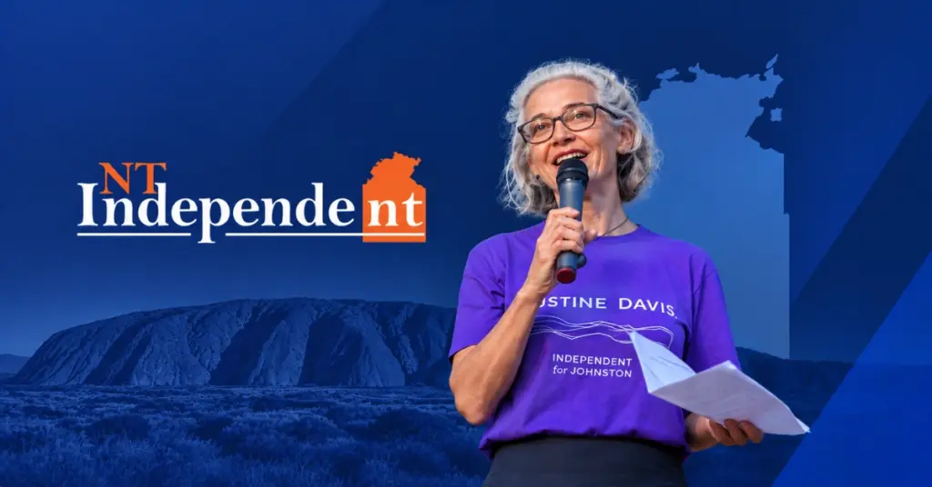 Justine Davis speaking into a microphone alongside the NT Independent logo and a Northern Territory backdrop in blue tones.