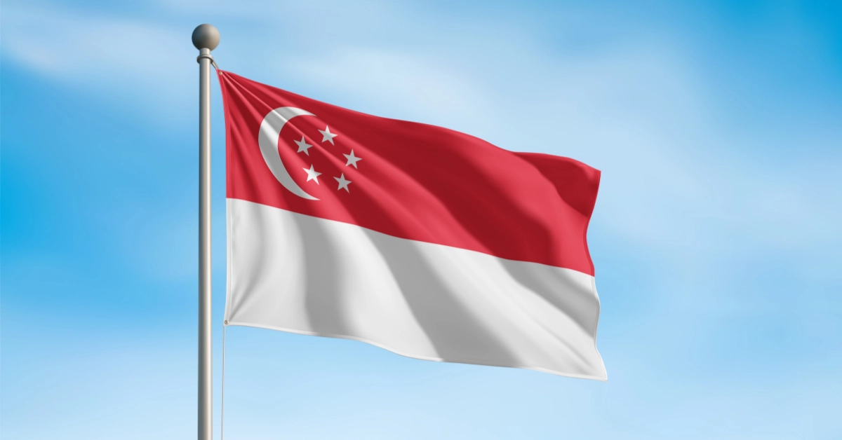 Singapore flag waving against a blue sky, featuring a white crescent and five stars above a white band.
