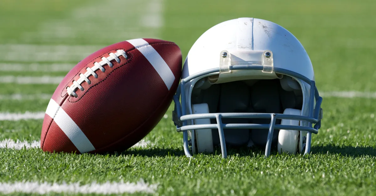 American football and a white helmet resting on a green field, representing US sports betting and athlete protection.
